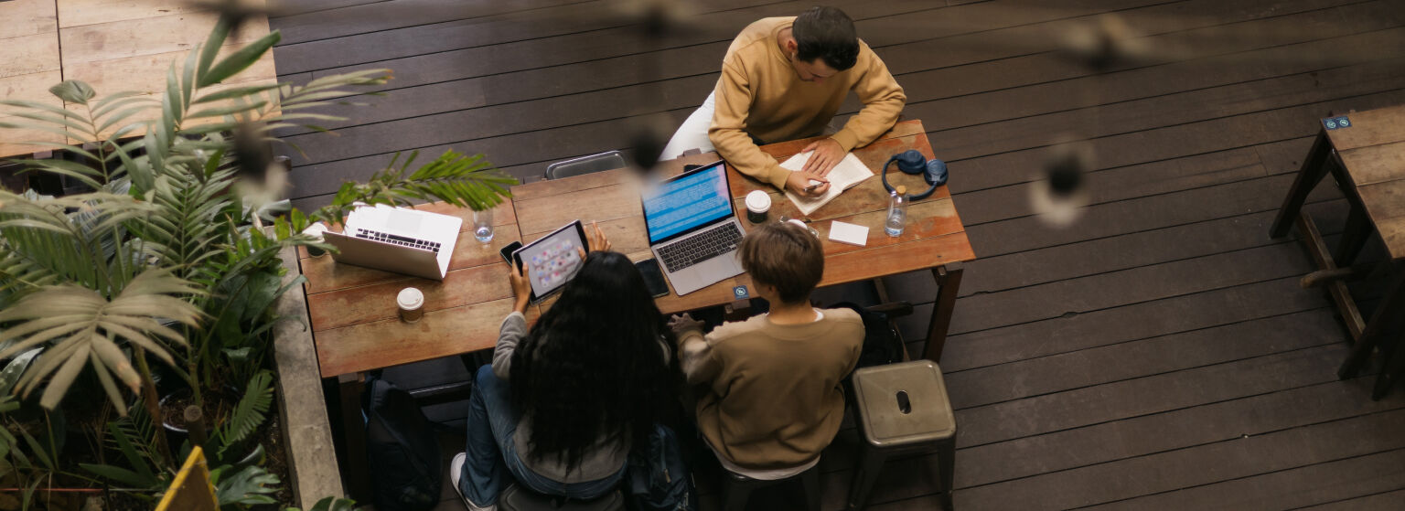 Three people working together at a table with laptops and notes.